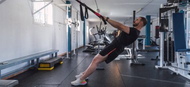 Spor salonunda TRX egzersizleri yapan genç bir adam. TRX eğitimi