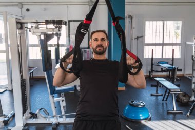Spor salonunda TRX egzersizleri yapan genç bir adam. TRX eğitimi