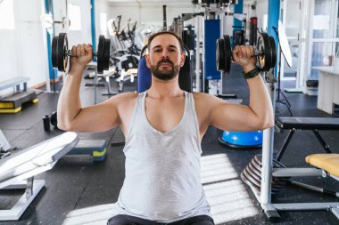 Dambıllarla omuz egzersizi yapan bir adam. Sağlık ve Sıhhat kavramı