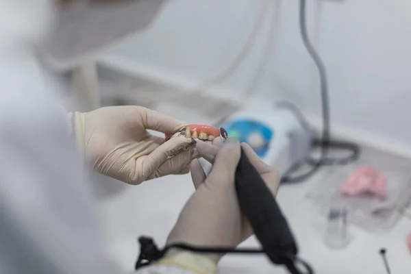 Hands of a dental technician with surgical mask and glasses polishing dentures on his table. health concept