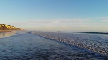 Dalgaları dağıtan bir kumsal ve denizin havadan çekilmiş videosu. Drone. Altın kumlu ve günbatımlı plajlar. Tatil kavramı