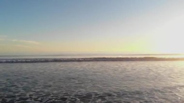 Dalgaları dağıtan bir kumsal ve denizin havadan çekilmiş videosu. Drone. Altın kumlu ve günbatımlı plajlar. Tatil kavramı