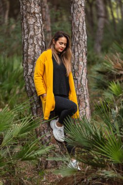 Ağaçta oturan bir kadın, ormanda sarı bir paltoyla ya da baharda park etmiş. Ağacın tepesindeki şapka