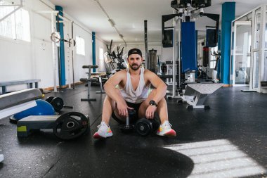 Salonda oturan genç adam, halterler dinleniyor..