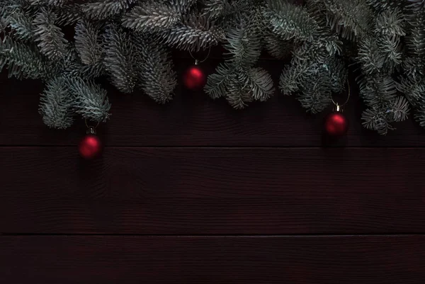 Koyu ahşap arka planda kırmızı takılar olan Noel ağacı dalları