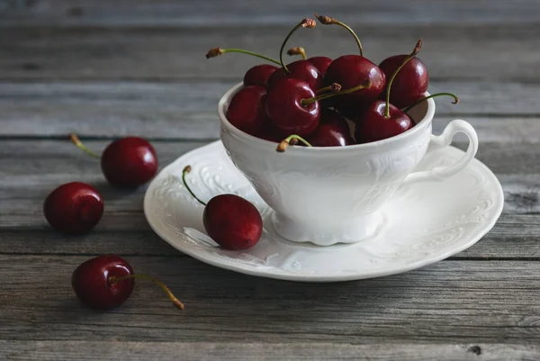 Beyaz çay fincanındaki kırmızı kirazlar eski ahşap arka planda, meyve natürmort