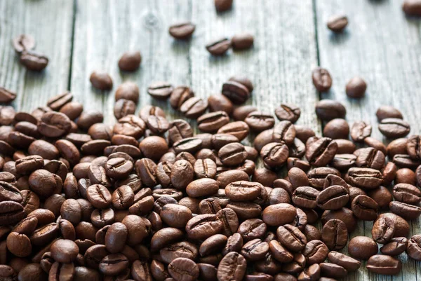 roasted coffee beans piled on bottom side of gray rustic wooden surface, backlit with natural light
