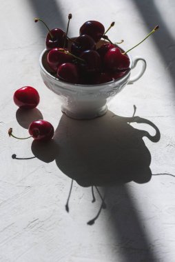 Beyaz porselen çay fincanındaki kırmızı kirazlar ışık ve gölge efektleriyle
