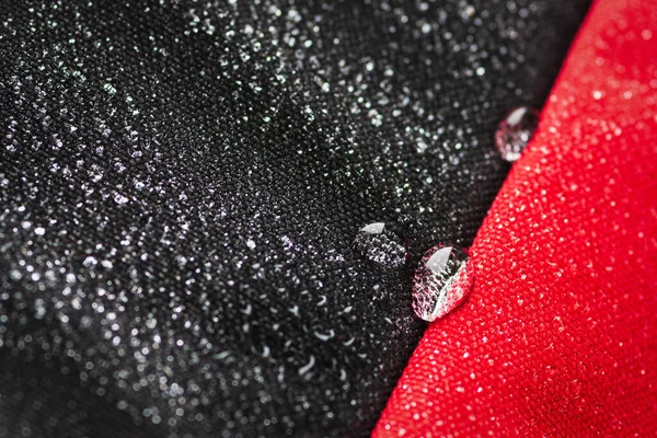 Drops of water on the water-resistant fabric of a waterproof bag of black and red cloth