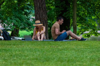 Yeşil Park 'taki ofisin dışında çalışan insanlar, çimlerin üzerinde oturan çift dizüstü bilgisayar kullanıyor, Moskova, 06.07.2020