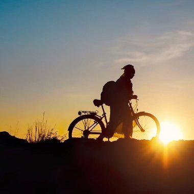 Solo gezgin - gün batımında bisikletli bir kadın, karanlık gökyüzüne karşı siluet