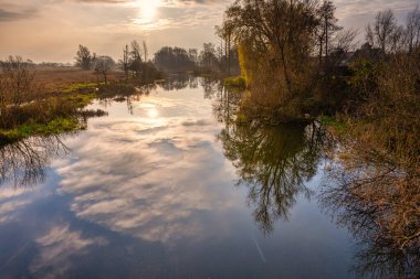 Nehirdeki ağaç ve bulut yansımalarının arka planda çekilmiş bir fotoğrafı. Arka planda güzel bir günbatımı gökyüzü. Fotoğraf İsveç 'in İskandinav ilçesinden.