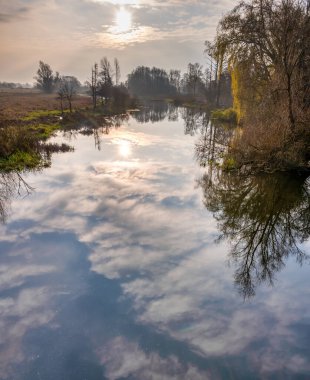 Nehirdeki ağaç ve bulut yansımalarının arka planda çekilmiş bir fotoğrafı. Arka planda güzel bir günbatımı gökyüzü. Fotoğraf İsveç 'in İskandinav ilçesinden.