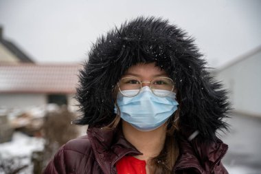 Koruyucu yüz maskesi takan, kışlık ceketli genç bir kız. Soğuk ve karlı bir resim