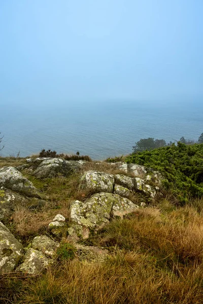 Una vista al mar desde una colina empinada un día brumoso. Hierba amarilla y piedras en primer plano. Foto de la reserva natural de Kullen, Scania, Suecia — Foto de Stock