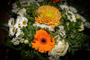 Bir buket cenaze çiçeğinin yakın plan fotoğrafı. Yeşil yapraklı beyaz, sarı ve turuncu çiçekler.