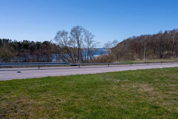 Ein offenes, mit Gras bedecktes Feld mit einer Straße und einer wunderschönen azur blauen Meeresbucht im Hintergrund. — Stockfoto