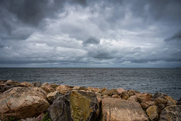 En vacker, dramatisk himmel över havet. Stenar i vågbrytare i förgrunden — Stockfoto