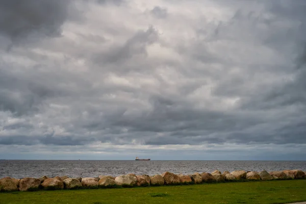 En vacker, dramatisk himmel över havet. En gräsmatta och stenar i en vågbrytare i förgrunden — Stockfoto