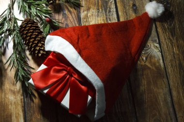 Kırmızı kurdeleli Noel hediyesi kutusu ve tahta arka planda Noel Baba şapkası. Noel arkaplanı. Noel kartı..