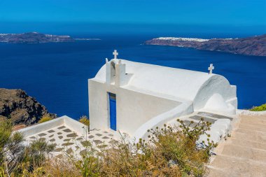 Yazın Santorini 'nin kalderasının üzerinden Oia ve Thirasia adalarına bakan bir uçurum kenarı şapeli.