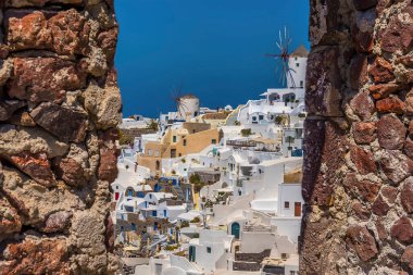 Oia 'nın yel değirmenleri ve beyaz binaları, Santorini yazları Oia Kalesi' nde taş bir pencereden bakıyordu.
