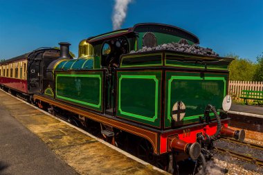 Güneşli bir yaz gününde Sussex, İngiltere 'de bir tren istasyonunda buhar boşaltan bir tren.