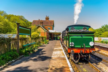 Güneşli bir yaz gününde Sussex, İngiltere 'de bir tren istasyonunda bekleyen bir buhar treni.
