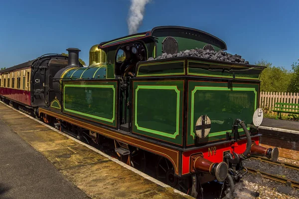 Güneşli bir yaz gününde Sussex, İngiltere 'de bir tren istasyonunda buhar boşaltan bir tren.