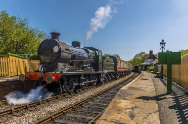 Güneşli bir yaz gününde İngiltere 'nin Sussex kentindeki tren istasyonundan buharlı trenler geçiyor.