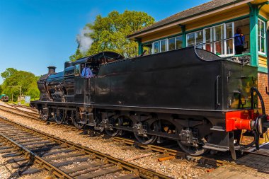 Güneşli bir yaz gününde İngiltere 'de bir demiryolu hattında sinyal kutusundan geçen bir buhar treni.