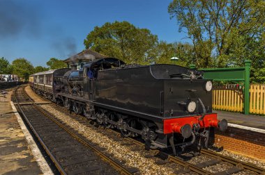 Güneşli bir yaz gününde İngiltere 'de bir demiryolu hattının tek bir bölümüne giren bir buhar treni.