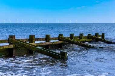 Yazın İngiltere 'nin Skegness plajındaki plaj savunmalarına yakın çekim. Ufukta bir rüzgar çiftliği görünüyor..