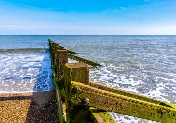 A view of the high and low sides of sea defense Groynes on Skegness beach with a wind farm  just visible on the horizon in summer