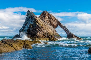 A view of waves crashing against the impressive Bow Fiddle Rock at Portknockie, Scotland on a summers day