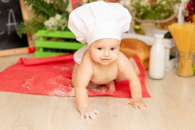 Küçük bir çocuk. Altı aylık bir kız. Mutfakta aşçı şapkası ve un içinde sürünüyor.