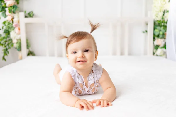 6个月大的小女孩躺在一个明亮美丽的房间里 白色的床上 身穿花边紧身衣 面带微笑 — 图库照片