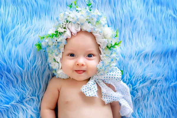 漂亮的小宝宝 戴着一顶花做的帽子 躺在蓝色的毛皮背景上 戴着花环 六个月大的小宝宝 — 图库照片