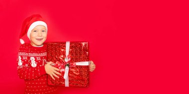 Kırmızı arka planda Noel Baba şapkası, afişi, yeni yıl konsepti ve Noel hediyesiyle izole edilmiş bir bebek.