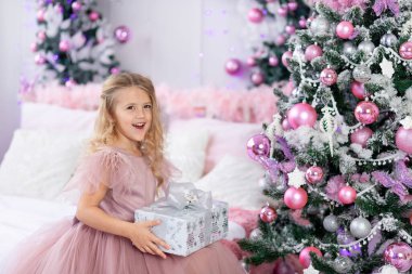 Bebek Noel ağacına yeni yıl ve noel konsepti olan pembe bir elbiseyle bir Noel hediyesi koyar.