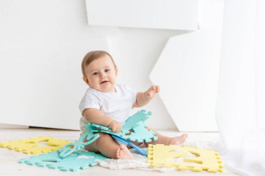 Altı aylık beyaz tişörtlü ve bez bezli şirin bir bebek. Parlak bir odada Mat 'te oynuyor. Mesaj atmak için yer var.