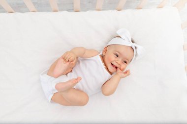 Mutlu bebek beyaz bir yatakta, çocuk odasındaki bir beşikte yatıyor.