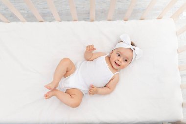 Mutlu bebek beyaz bir yatakta, çocuk odasındaki bir beşikte yatıyor.
