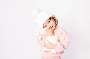 Kışın giyinmiş küçük bir kız beyaz arka planda bir tavşan tutuyor. Yeni yılın konsepti, metin için alan