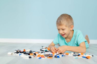 Bir çocuk mavi arka planda bir lego evi yapımcısıyla oynuyor.