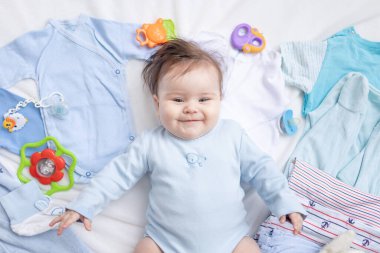 Mavi elbiseli bir bebek çocuk aksesuarları ve kıyafetleri arasında yatıyor.