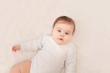 Sevimli bir bebek. Beyaz bir kıyafetle altı ay bir karyolada yatıyor.