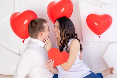 Sevgililer Günü 'nde, güzel bir kızla birlikte bir adam büyük kırmızı bir kalp taşıyan sevgi dolu bir bakışla birbirlerine bakar.