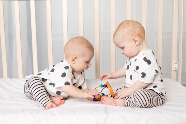 2人の双子の赤ちゃんがベビーベッドで遊んでいます弟と妹の子供の関係の概念は 子供は他の子供からおもちゃを取ります — ストック写真
