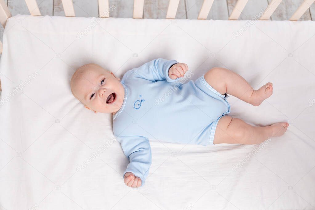 laughing baby lies in the crib, cute little boy of six months lies in the nursery on the bed and laughs